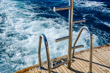Metal staircase for descent into the water and wave trace with white foam on water surface behind of fast moving yachtの写真素材