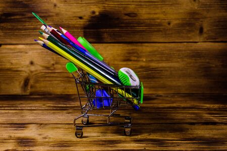 Small shopping cart with different school stationery on rustic wooden background. Back to school conceptの写真素材