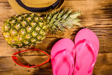 Pineapple, straw hat, sunglasses and flip flops on rustic wooden table. Summer vacations. Top viewの写真素材