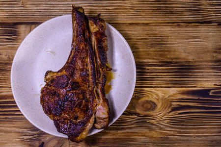 Plate with roasted ribeye steak on rustic wooden table. Top view