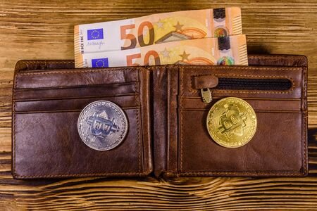 Brown leather wallet with fifty euro banknotes and bitcoins on wooden background. Top viewの写真素材