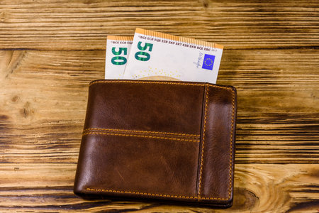 Brown leather wallet with fifty euro banknotes on wooden background