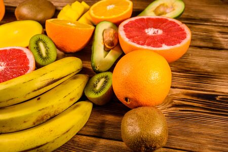 Still life with exotic fruits. Bananas, mango, oranges, avocado, grapefruit and kiwi fruits on rustic wooden tableの写真素材
