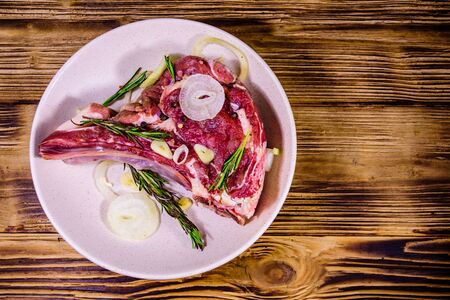 Raw ribeye steak, spices, rosemary, onion and garlic in ceramic plate on rustic wooden table. Top viewの写真素材