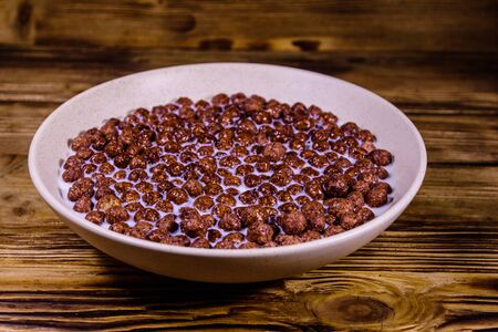 Ceramic plate with chocolate cereal balls in milk on rustic wooden tableの写真素材
