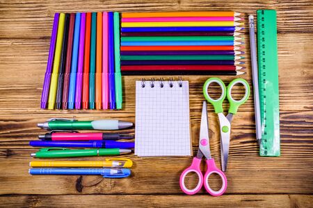 Different school stationeries (pens, notepad, pencils, felt tip pens, scissors and ruler) on wooden background. Top viewの写真素材
