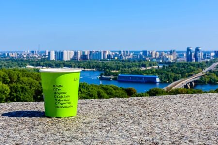 Paper glass of coffee on stone parapet in front of Kiev cityscape. View on residential districts on left bank of river Dnieper in Kiev, Ukraineの写真素材