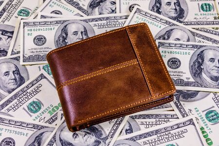 Closed brown leather wallet on one hundred dollar banknotesの写真素材