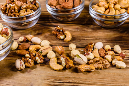 Various nuts (almond, cashew, hazelnut, pistachio, walnut) in glass bowls on wooden table....