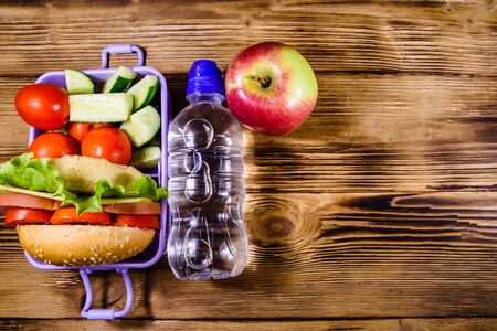 Ripe apple, bottle of water and lunch box with hamburger, cucumbers and tomatoes on rustic wooden table. Top viewの写真素材