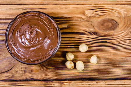 Glass bowl with chocolate spread on wooden table. Top view