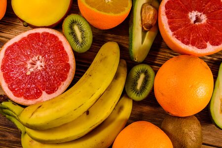 Still life with exotic fruits. Bananas, mango, oranges, avocado, grapefruit and kiwi fruits on rustic wooden table. Top viewの写真素材