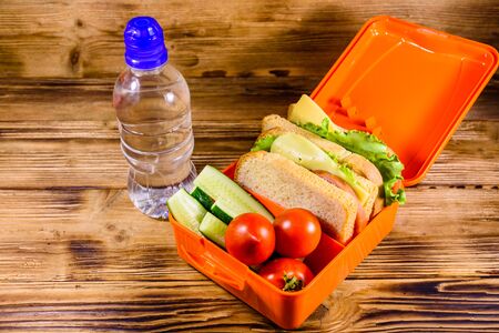 Bottle of water and lunch box with sandwiches, cucumbers and tomatoes on rustic wooden tableの写真素材