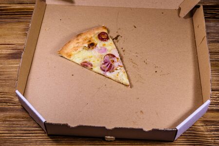 Last piece of pizza with sausages, ham and parmesan cheese in cardboard boxの写真素材