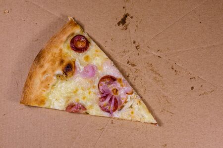 Last piece of pizza with sausages, ham and parmesan cheese in cardboard boxの写真素材
