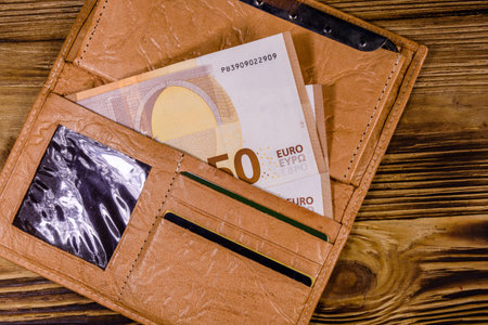Brown leather wallet with fifty euro banknotes on wooden background. Top view