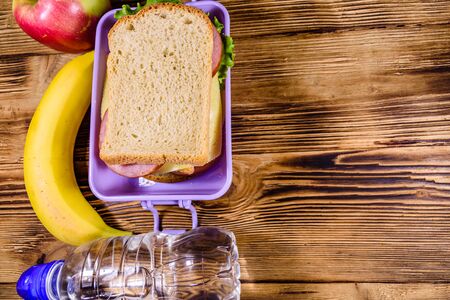 Ripe apple, banana, bottle of water and lunch box with sandwiches on wooden table. Top viewの写真素材