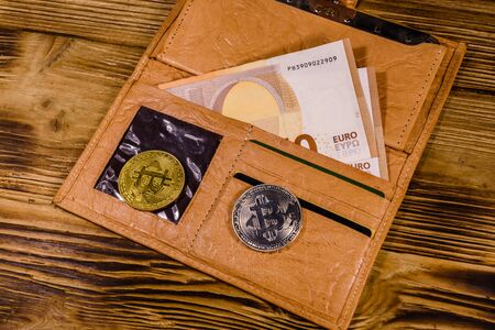 Brown leather wallet with fifty euro banknotes and bitcoins on wooden backgroundの写真素材