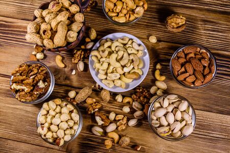 Various nuts (almond, cashew, hazelnut, pistachio, walnut) in bowls on wooden table. Vegetarian meal. Healthy eating concept. Top viewの写真素材