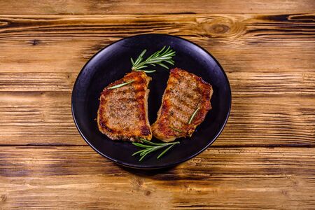 Plate with roasted steaks and rosemary twigs on wooden tableの写真素材