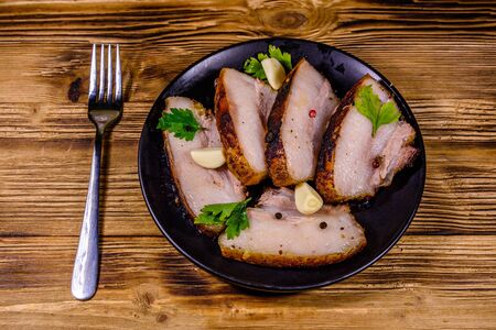 Slices of baked pork belly, garlic and parsley on black plateの写真素材