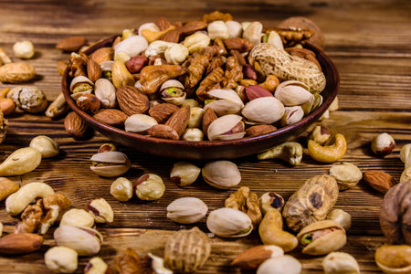 Various nuts (almond, cashew, hazelnut, pistachio, walnut) in ceramic plate on wooden table....