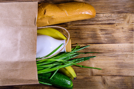 Paper bag with different food from grocery on wooden table. Supermarket shopping concept. Top view