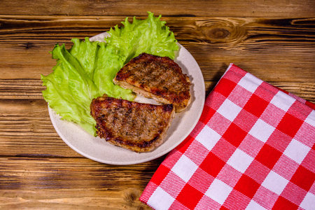 Plate with roasted steaks and rosemary twigs on wooden table