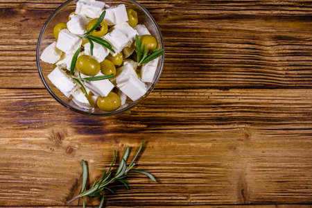 Chopped feta cheese, rosemary and olives in glass bowl on wooden table. Top viewの写真素材