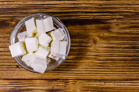 Chopped feta cheese in glass bowl on wooden table. Top view