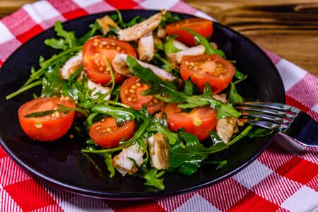 Roasted chicken breasts and salad with arugula and cherry tomatoes in black plateの写真素材