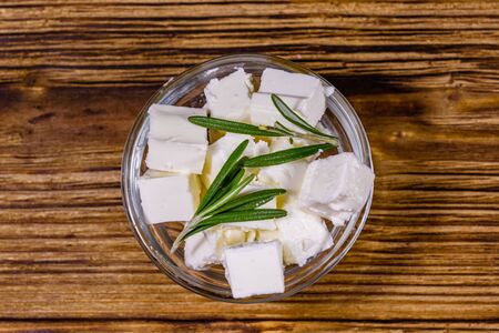 Chopped feta cheese and rosemary in glass bowl on wooden table. Top viewの写真素材
