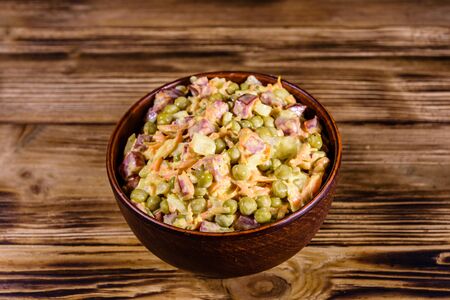 Salad with sausage, green pea, onion and carrot in glass bowl on rustic wooden tableの写真素材