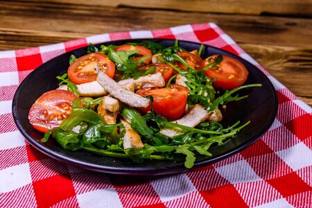 Roasted chicken breasts and salad with arugula and cherry tomatoes in black plateの写真素材