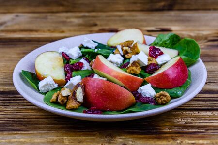 Salad with spinach leaves, feta cheese, cranberries, walnuts and apple in ceramic plateの写真素材
