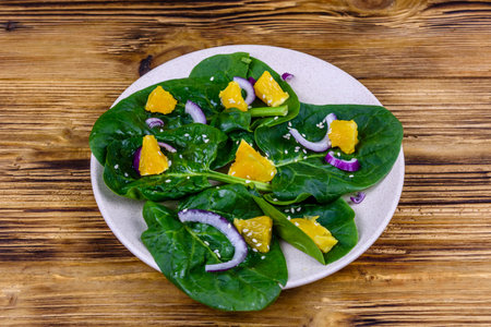 Salad with spinach leaves, pieces of orange, sesame seeds and onion in ceramic plateの写真素材