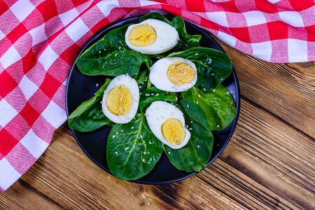 Spinach leaves and halved boiled eggs on black plate. Top viewの写真素材