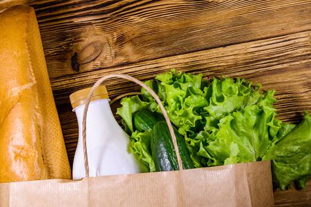 Paper bag with different food from grocery on wooden table. Supermarket shopping concept. Top viewの写真素材