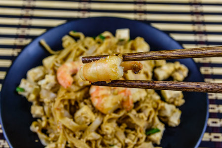 Black plate with pad thai on bamboo mat. Chopsticks with shrimp