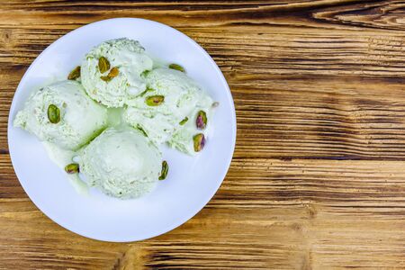 Glass bowl with pistachio ice cream balls and nuts on wooden table. Top viewの写真素材