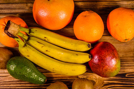 Still life with exotic fruits. Bananas, mango, oranges, avocado, grapefruit and kiwi fruits on rustic wooden table. Top viewの写真素材