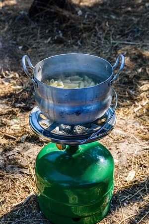 Pasta cooking in aluminum pan on portable gas stove. Bushcraft or camping conceptの写真素材