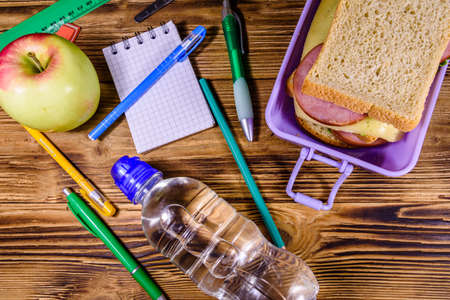 Bottle of water, ripe apple, different stationeries and lunch box with sandwiches on wooden table. Top viewの写真素材