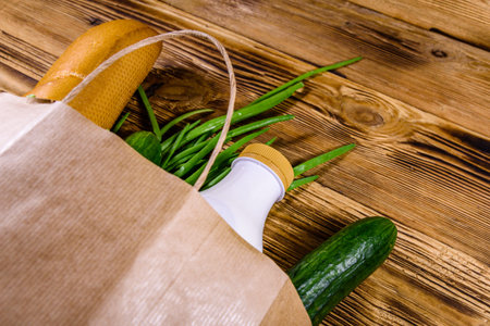 Paper bag with different food from grocery on wooden table. Supermarket shopping concept