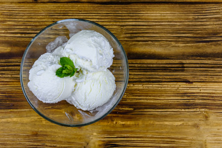 Glass bowl with ice cream balls and mint leaf on wooden table. Top view