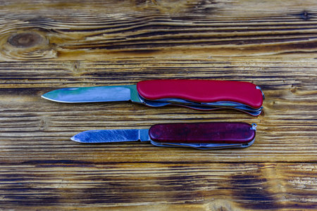Two unfolded all purpose red pocket knives on a wooden background