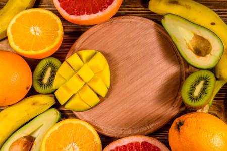 Still life with exotic fruits and cutting board. Bananas, mango, oranges, avocado, grapefruit and kiwi fruits on rustic wooden table. Top viewの写真素材