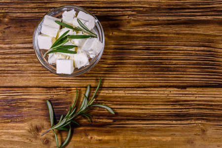 Chopped feta cheese and rosemary in glass bowl on wooden table. Top viewの写真素材