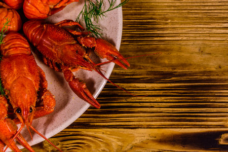 Plate with boiled crayfishes on rustic wooden table. Top view