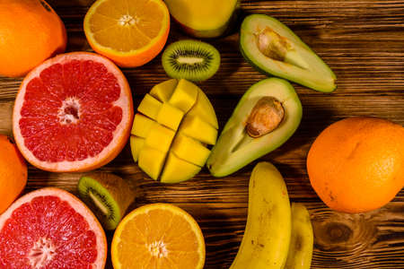 Still life with exotic fruits. Bananas, mango, oranges, avocado, grapefruit and kiwi fruits on rustic wooden table. Top viewの写真素材